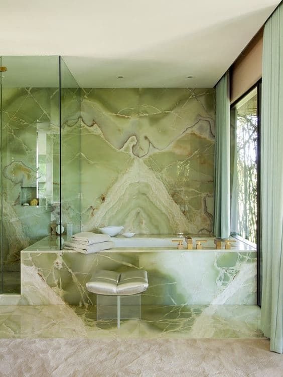 Elegant bathroom featuring Green Onyx marble on walls, countertop, and bathtub surround, with large windows bringing in natural light.