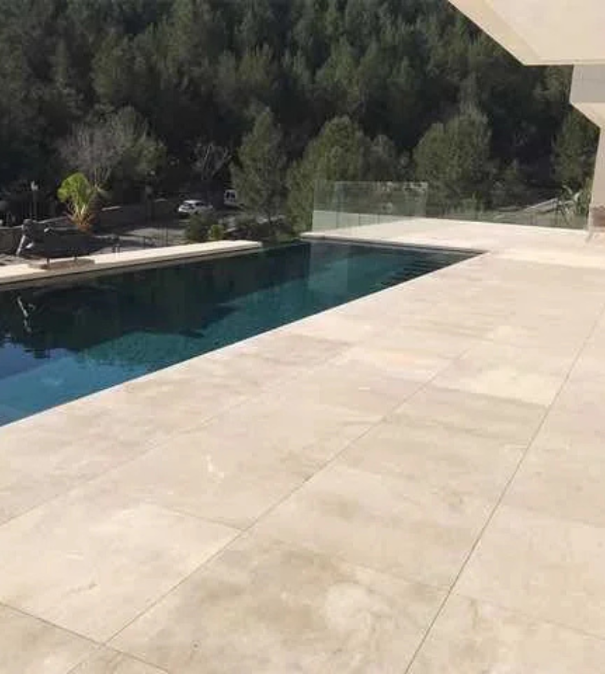 Luxurious outdoor poolside deck finished with Crema Levante Marble, surrounded by scenic greenery and modern architectural lines