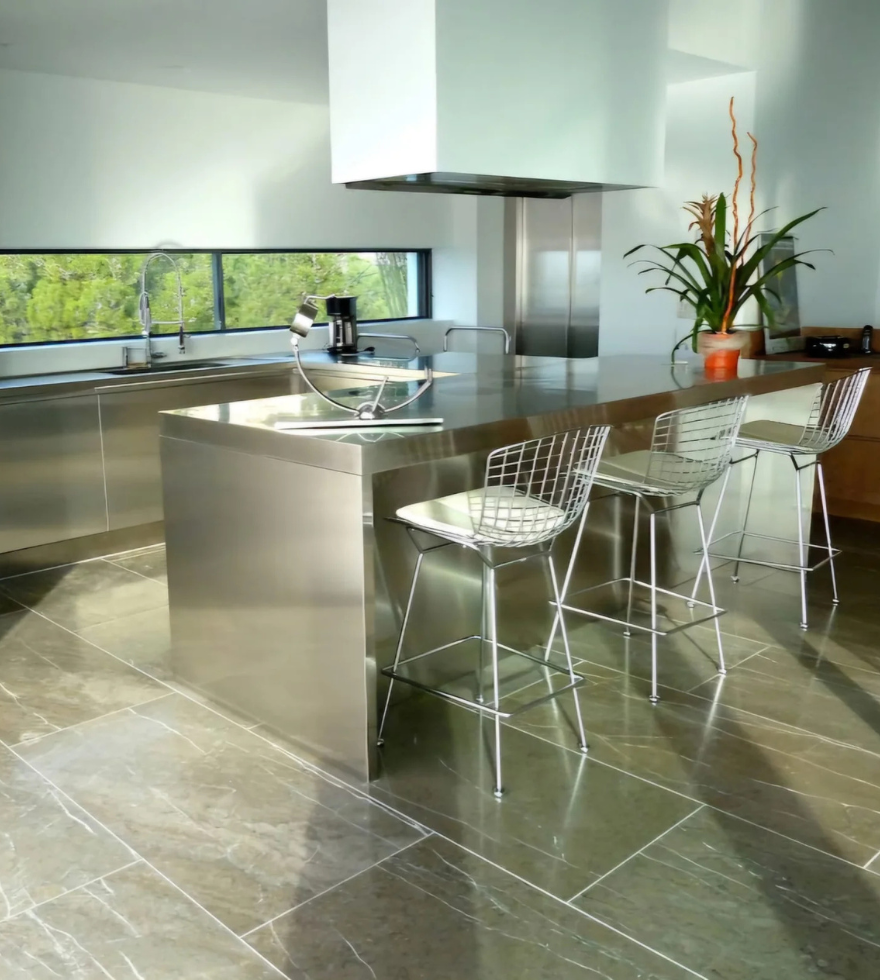 Modern kitchen interior featuring glossy Sierra Elvira Marble flooring, with stainless steel countertops, minimalist decor, and natural light streaming through large windows.
