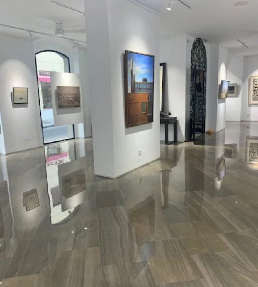 Art gallery with highly polished dark brown marble flooring featuring natural veining, surrounded by white walls and contemporary paintings.