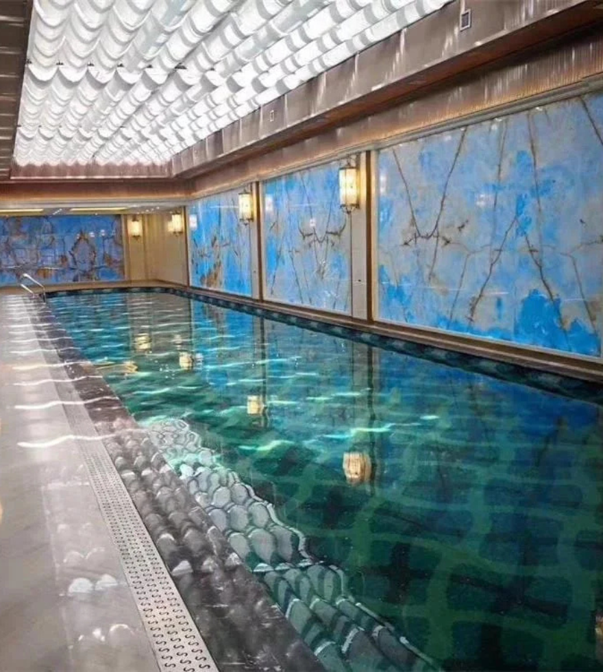 Luxurious indoor swimming pool lined with large panels of Blue Onyx marble on the walls, featuring bold blue tones and golden veining for an opulent spa-like ambiance.