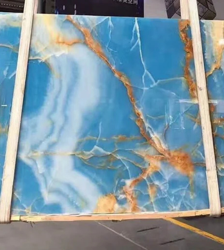 Polished Blue Onyx marble slab with striking white waves and vivid golden-orange veining, displayed vertically in a warehouse setting.