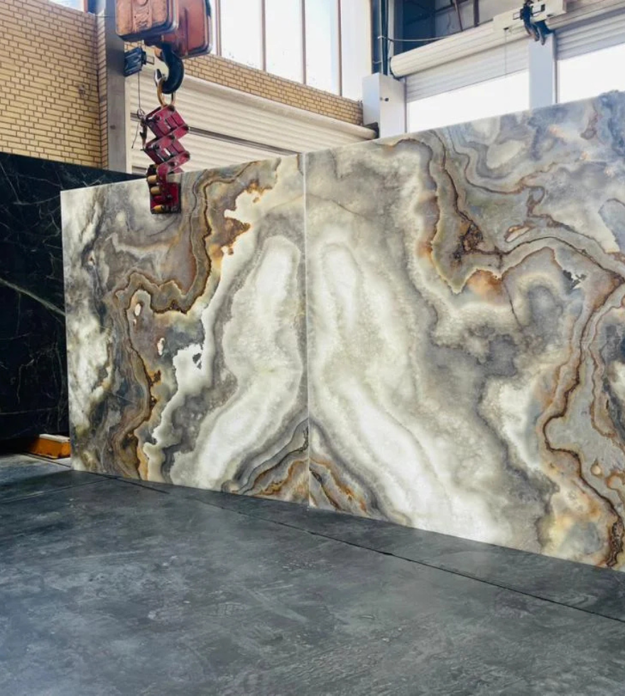 Polished slab of Cloudy Onyx Marble with intricate white, grey, and amber veining displayed in an indoor stone showroom.