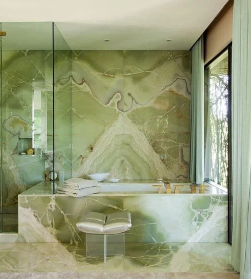 Luxurious bathroom interior featuring Green Onyx Marble walls and bathtub, showcasing intricate green and white veining, complemented by floor-to-ceiling windows and modern glass partitions.