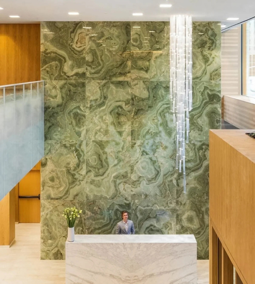 Grand reception area featuring a striking Green Onyx Marble accent wall with intricate swirling patterns in green and cream, creating a luxurious and natural focal point.