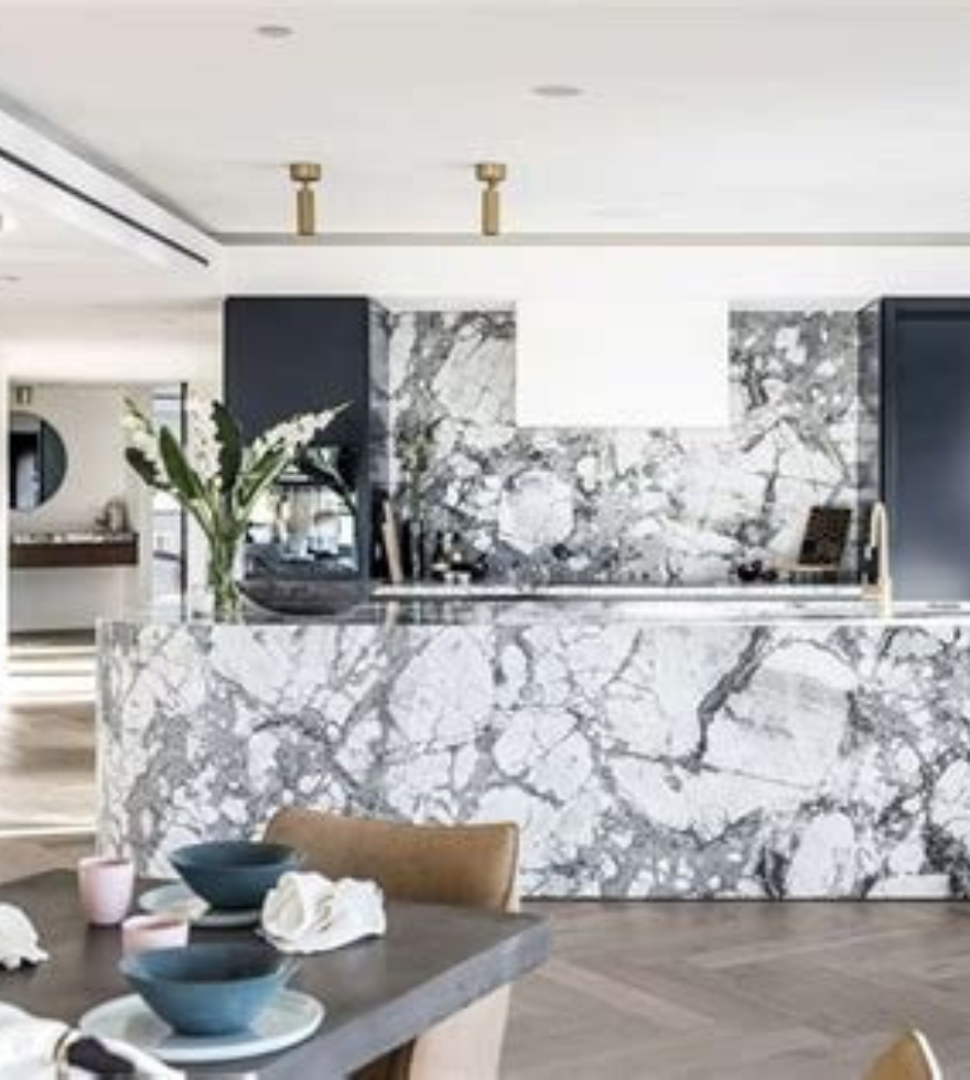Contemporary kitchen design showcasing bold White Dover Marble on the island and backsplash, with dramatic black veining, paired with gold fixtures and elegant dining accents.