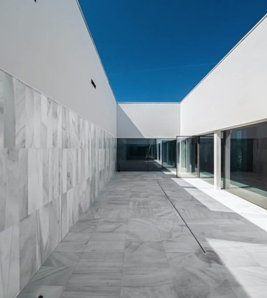 Contemporary architectural courtyard featuring White Macael Marble flooring and cladding, with clean geometric lines, glass walls, and a vivid blue sky backdrop.