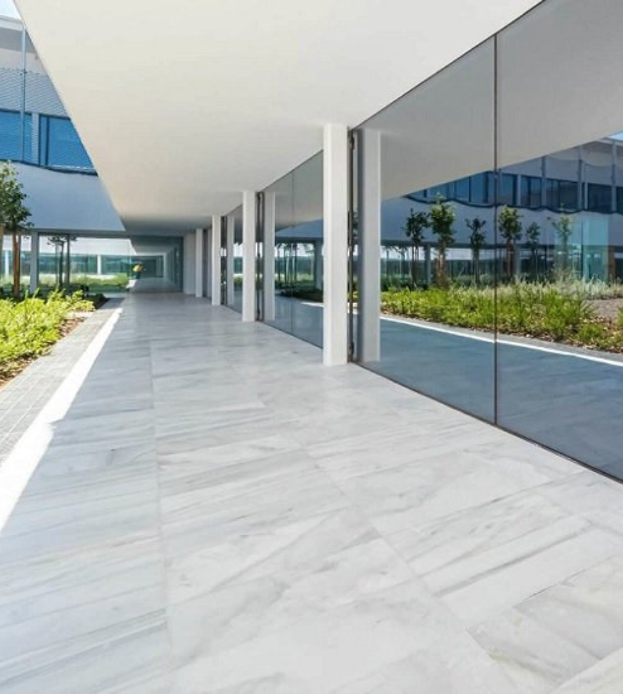 Modern commercial building exterior with expansive White Macael Marble flooring, sleek glass walls, and a minimalist design surrounded by landscaped greenery.