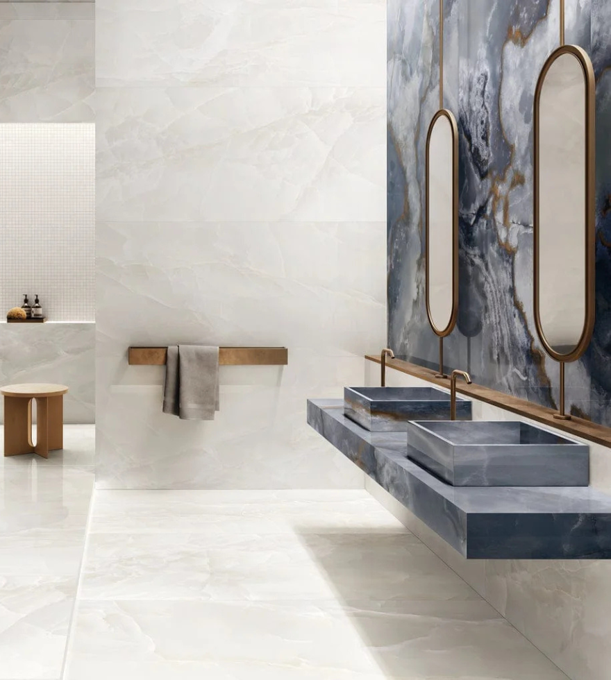 Elegant bathroom featuring sleek White Onyx marble walls and flooring, paired with bold dark stone countertops and modern brass-framed mirrors.